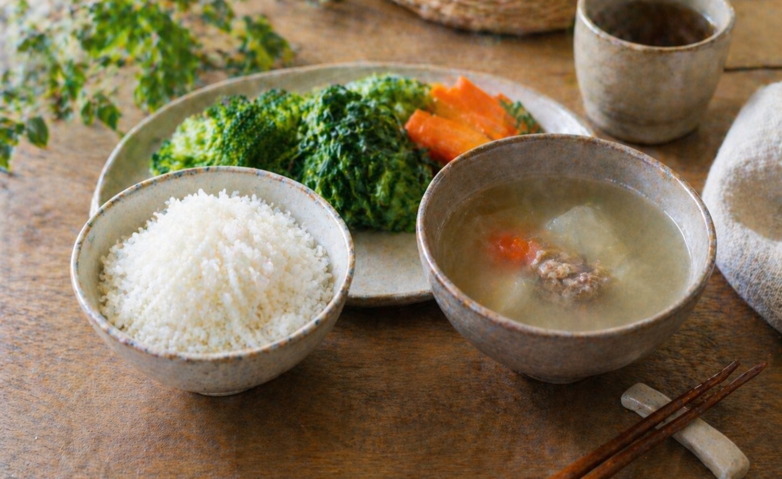 Assiette de repas simple et chaud composée de riz, légumes cuits à la vapeur et bouillon clair, posée sur une table avec des baguettes